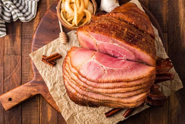 A ham is sitting on a wooden cutting board.