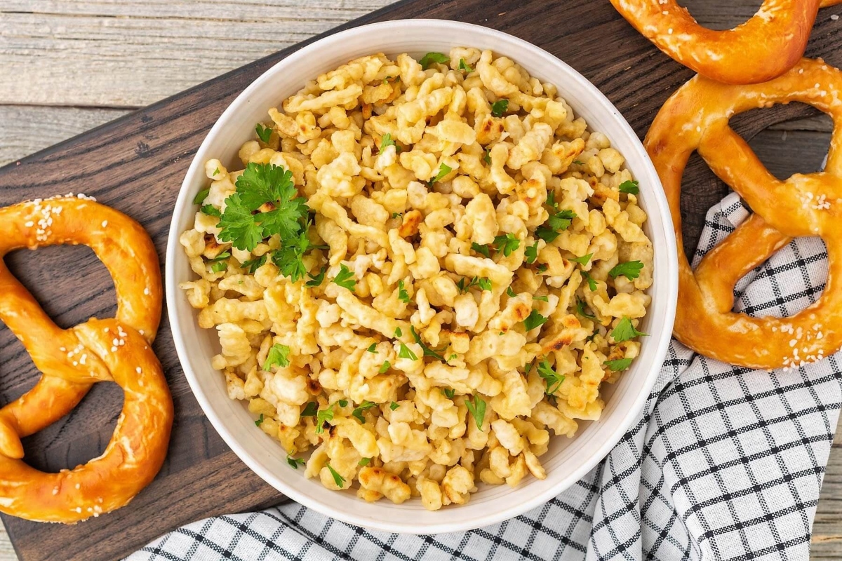 A German-inspired bowl of macaroni and cheese with pretzels on a wooden cutting board.