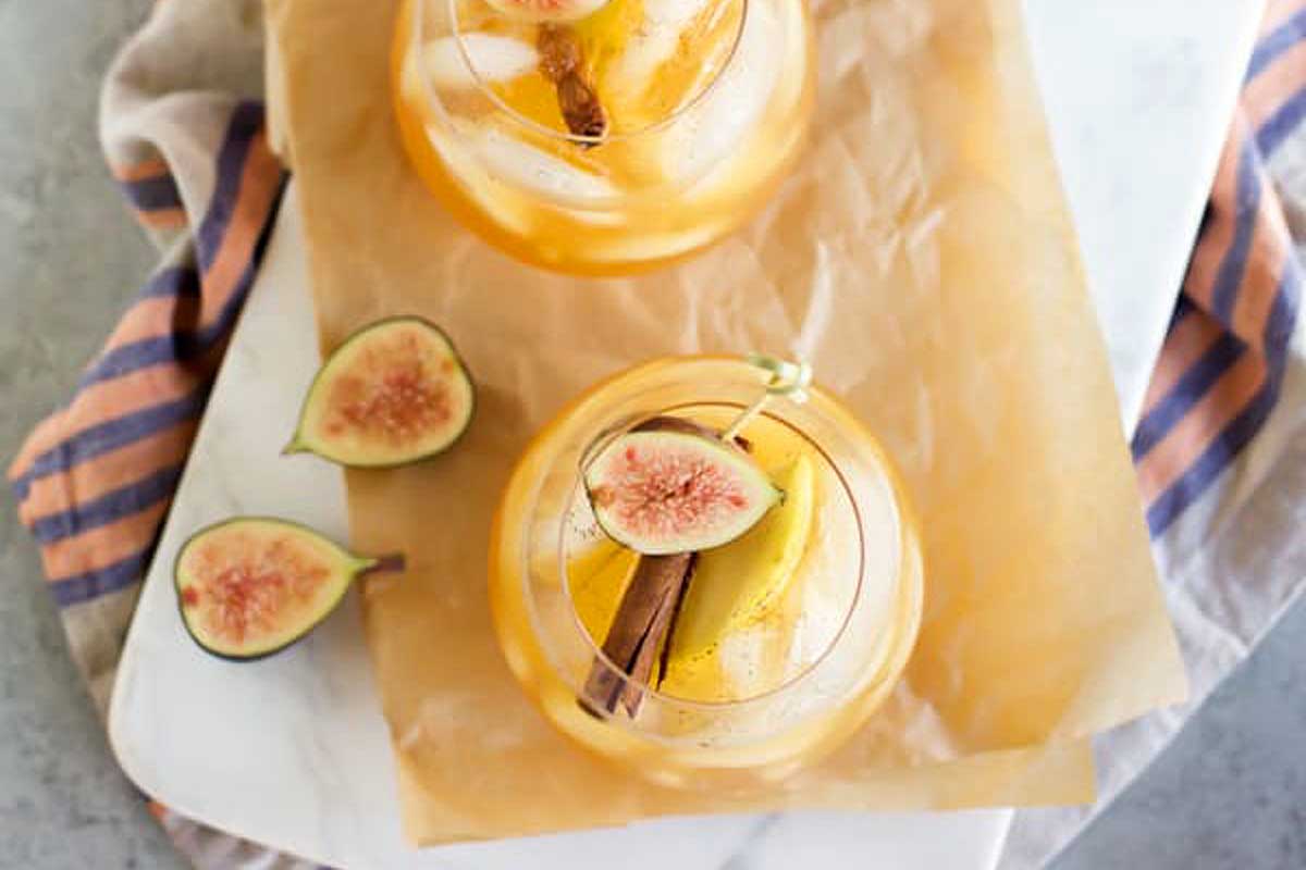 Fall cocktail featuring two glasses of orange sangria with figs and cinnamon.