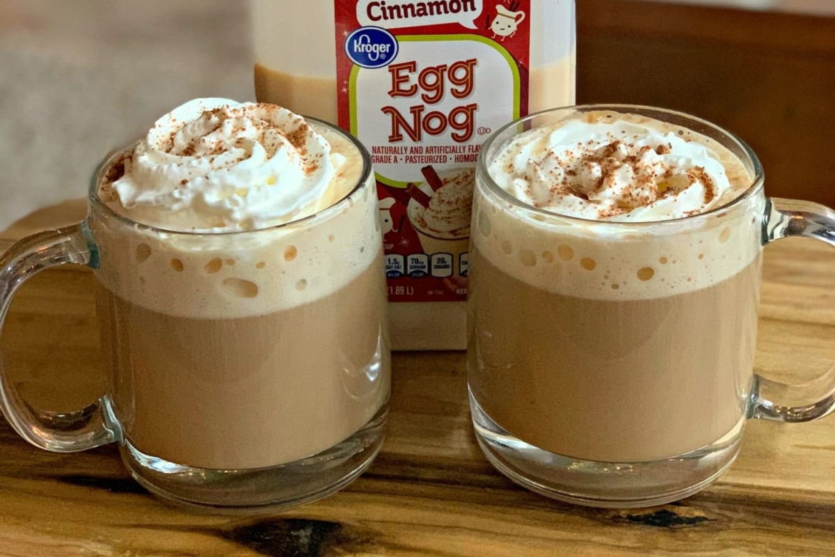 Two mugs filled with delicious, homemade eggnog topped with fluffy whipped cream.