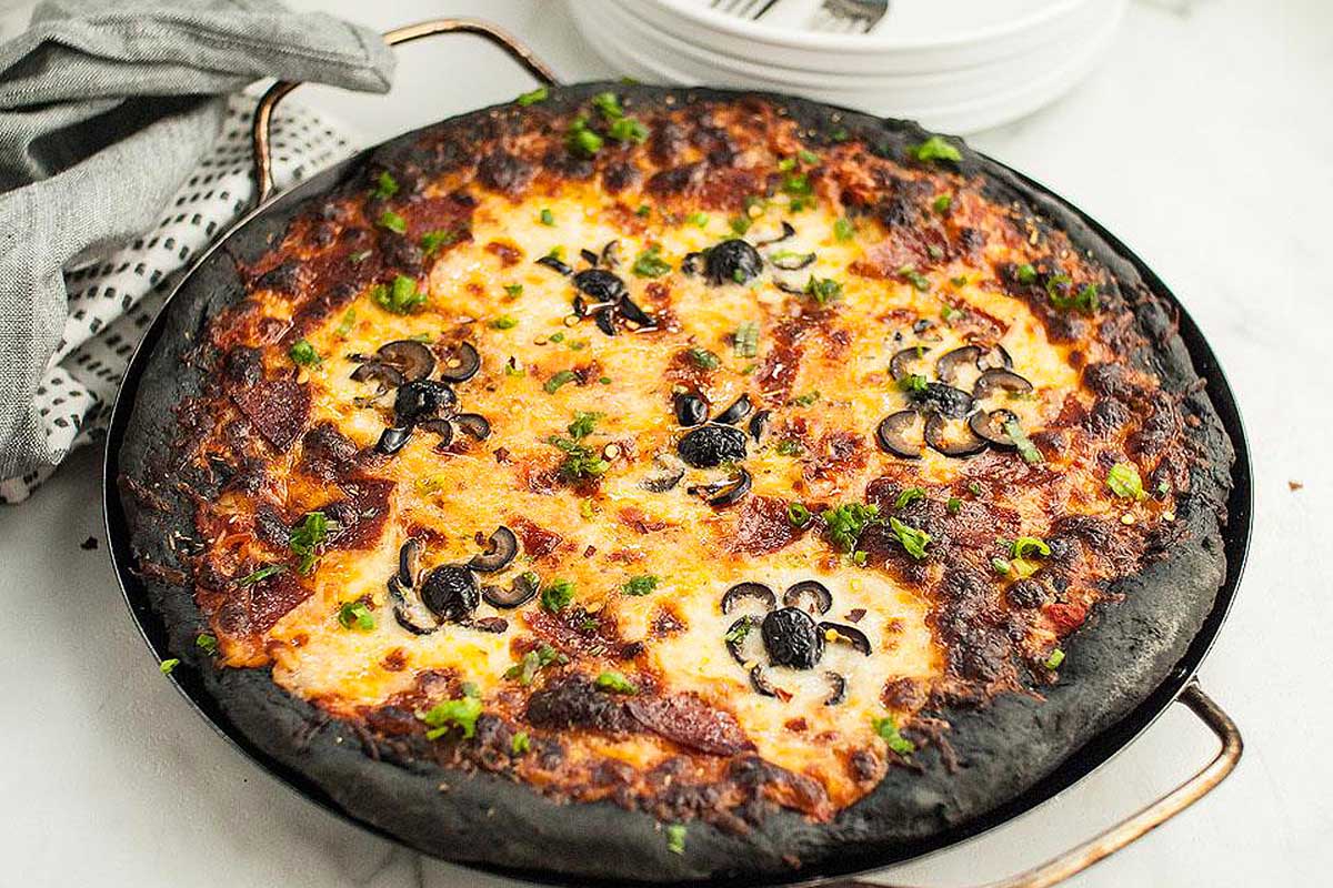 A pizza in a pan on a marble table.