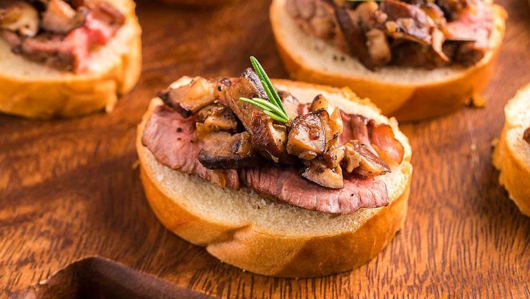 Beef and mushroom crostini, perfect for any occasion, beautifully displayed on a wooden cutting board with rosemary sprigs.
