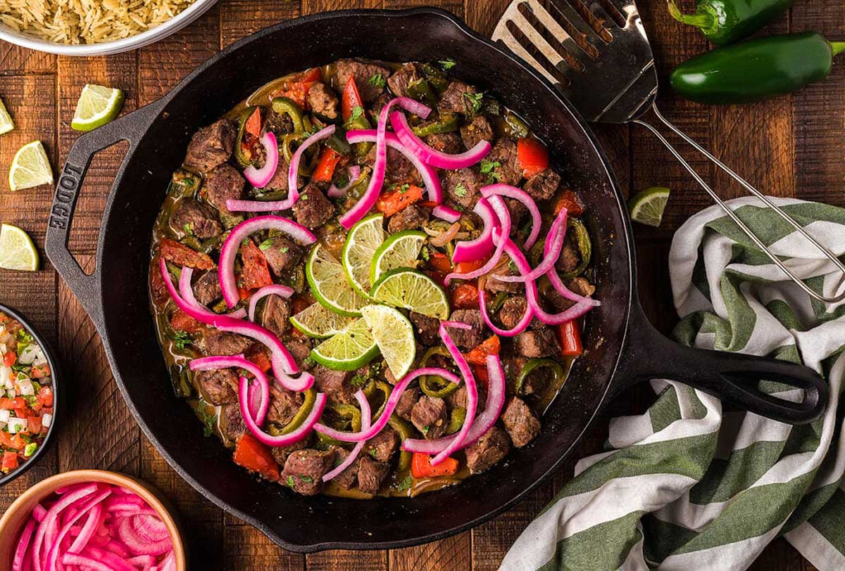A mexican skillet with meat and vegetables on a wooden table.