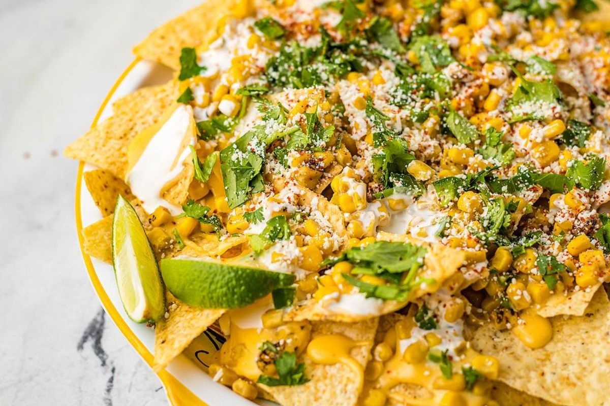 Corn nachos in a yellow bowl with lime and cilantro.