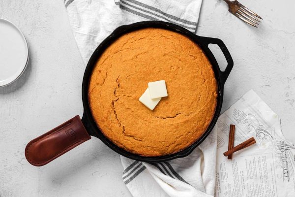 Cheap cornbread in a cast iron skillet with butter, perfect for Thanksgiving potluck dishes.
