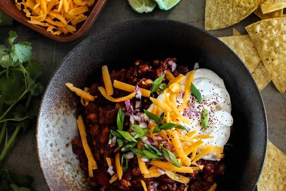 Chili in a bowl with sour cream and tortilla chips.