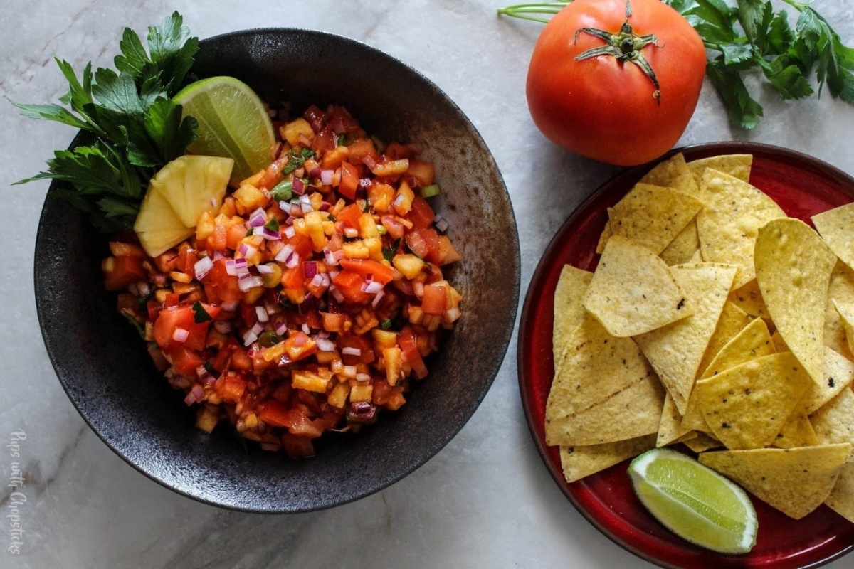 A bowl of salsa and tortilla chips on a marble table.