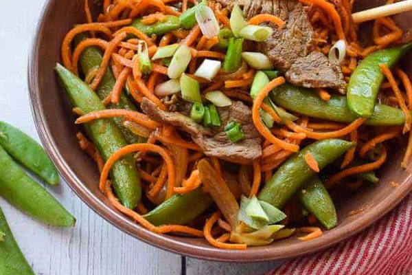 A bowl of beef and carrot noodles with chopsticks.