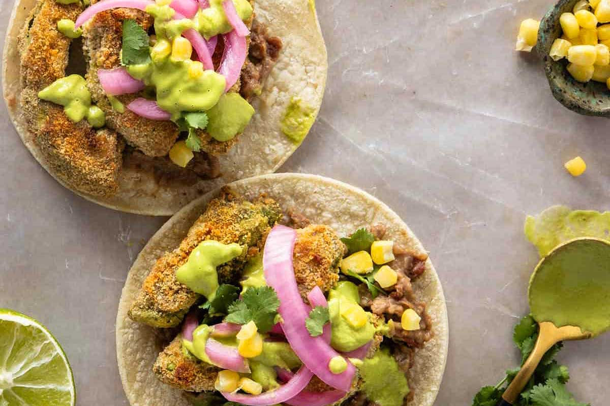Two tacos topped with avocado, onion and cilantro.