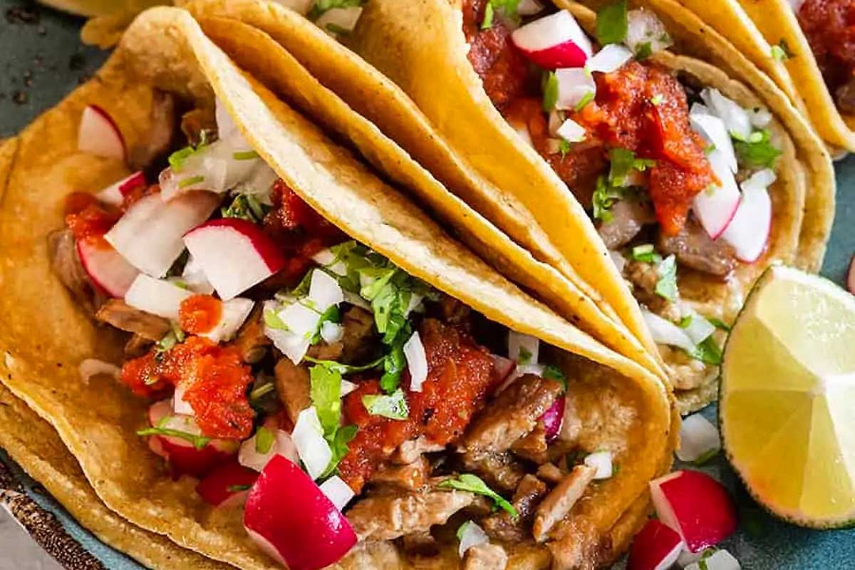Three tacos on a plate with radishes and limes.
