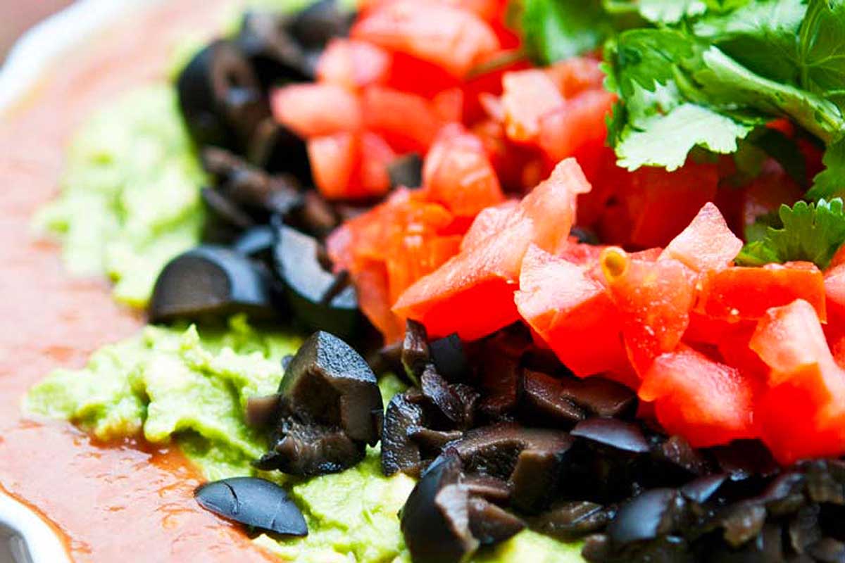 Guacamole with black beans and tomatoes on a white plate.