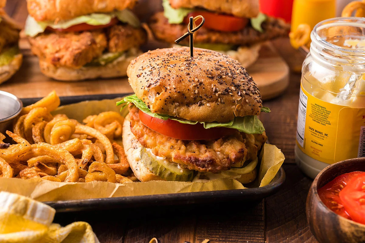 Chicken burgers served on a wooden table, accompanied by onion rings.