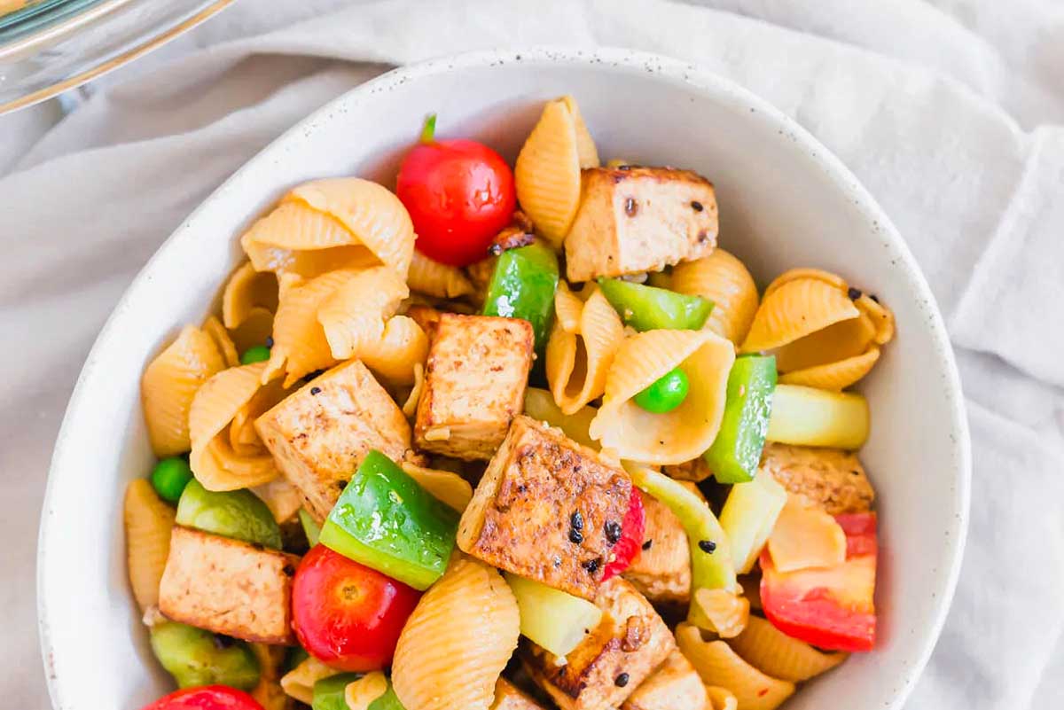 A white bowl with tofu and vegetables in it, resembling a light and refreshing pasta salad.