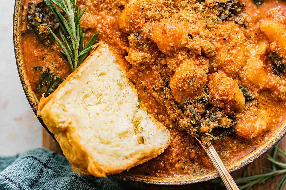 A bowl of stew with bread and sprigs of sage.