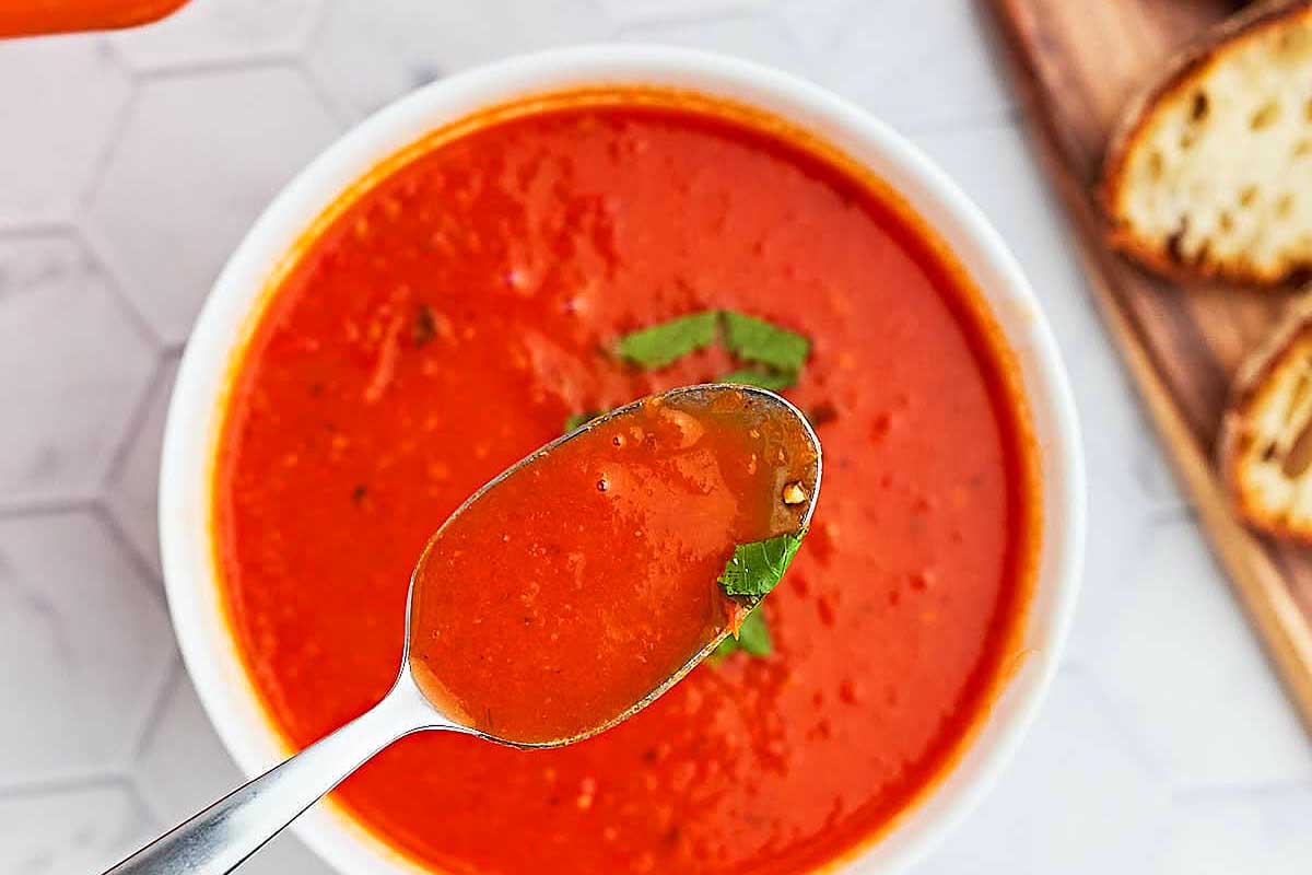 A bowl of tomato soup with a slice of bread.