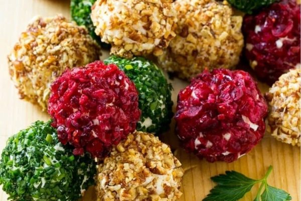 Cranberry granola bites and cheese ball on a wooden cutting board.