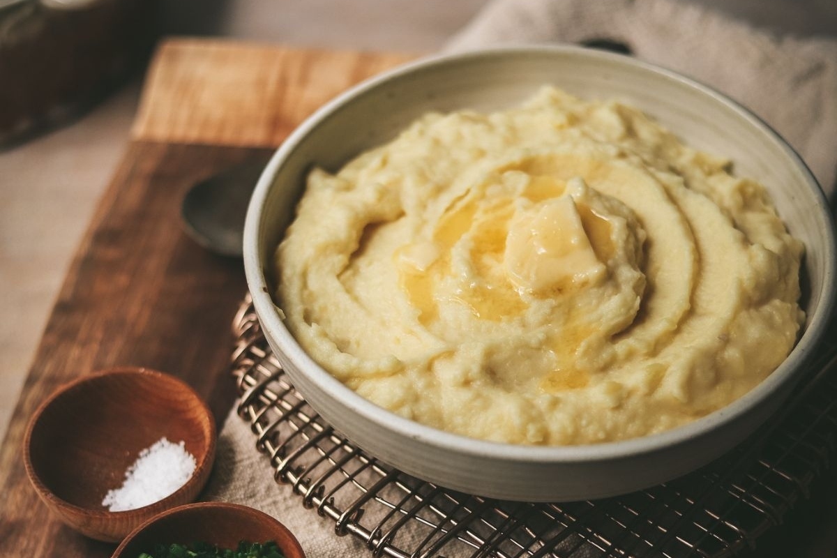 A bowl of mashed potatoes on a wooden cutting board, ready to be served as a delicious side dish.