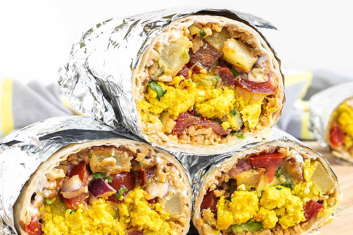 Breakfast burritos wrapped in foil on a cutting board.