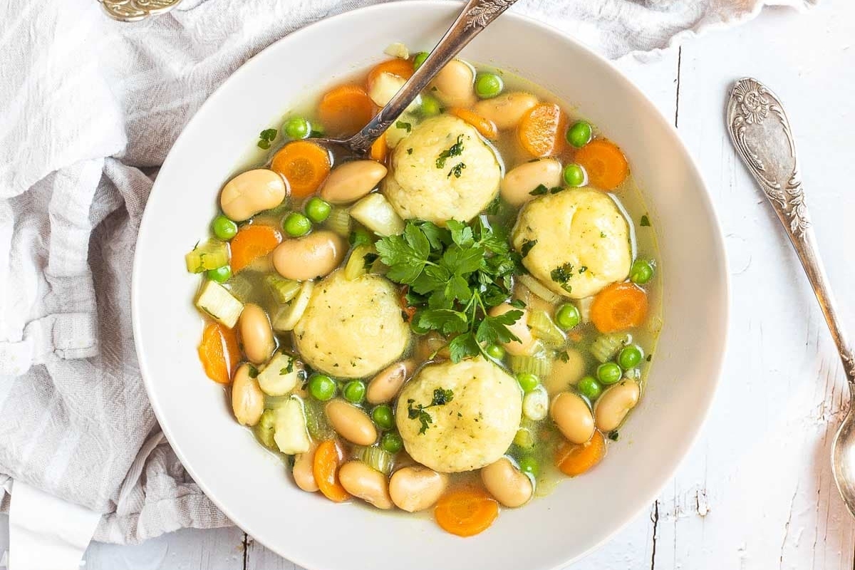 A bowl of soup with dumplings and frozen peas.