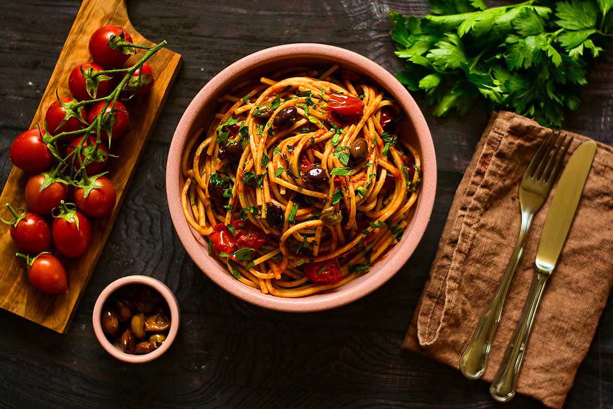 A bowl of spaghetti with tomatoes and herbs on a wooden table.