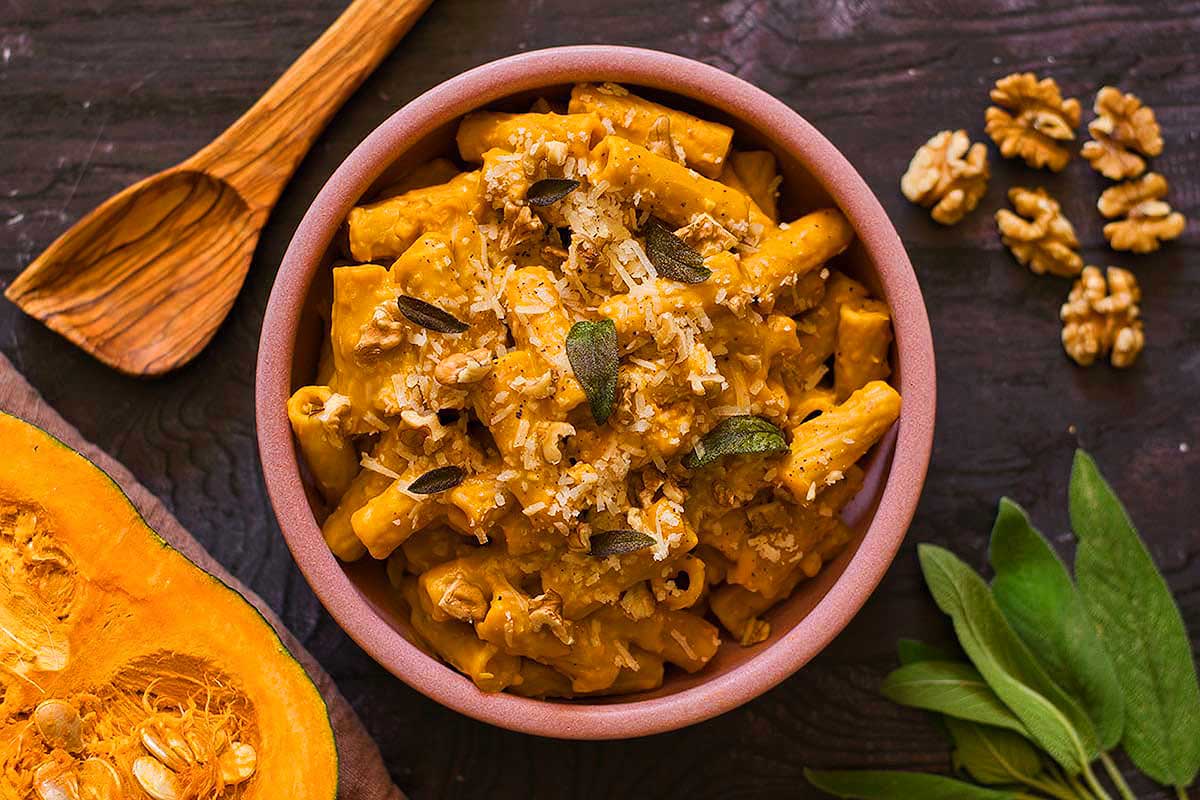 A bowl of pasta with pumpkin seeds and walnuts.