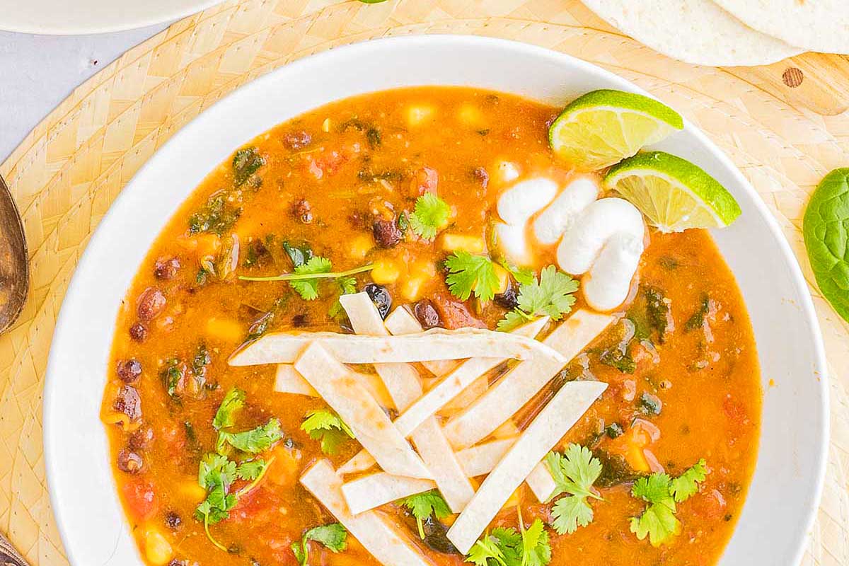 A bowl of mexican black bean soup with tortillas and lime.