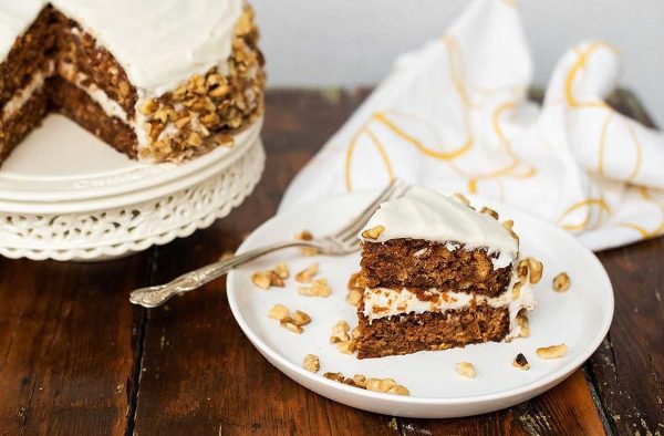 A slice of carrot cake with icing and nuts on a plate.