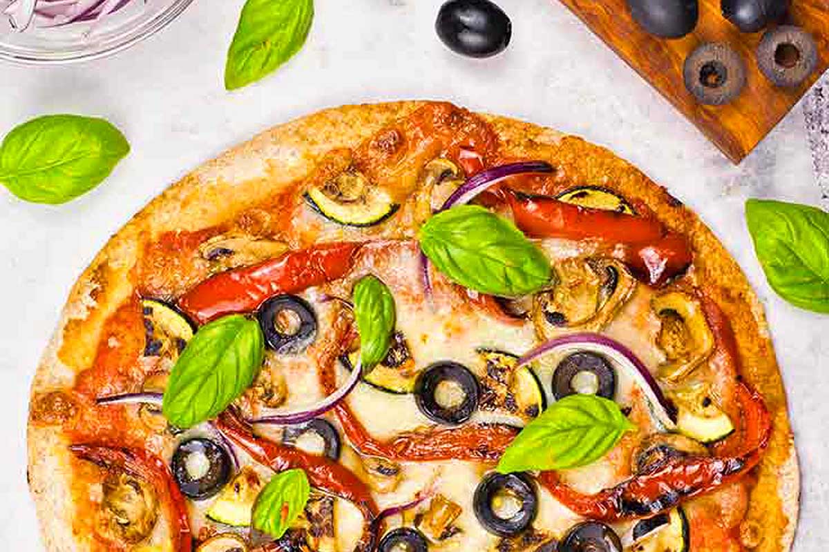 A pizza with vegetables and olives on a table.