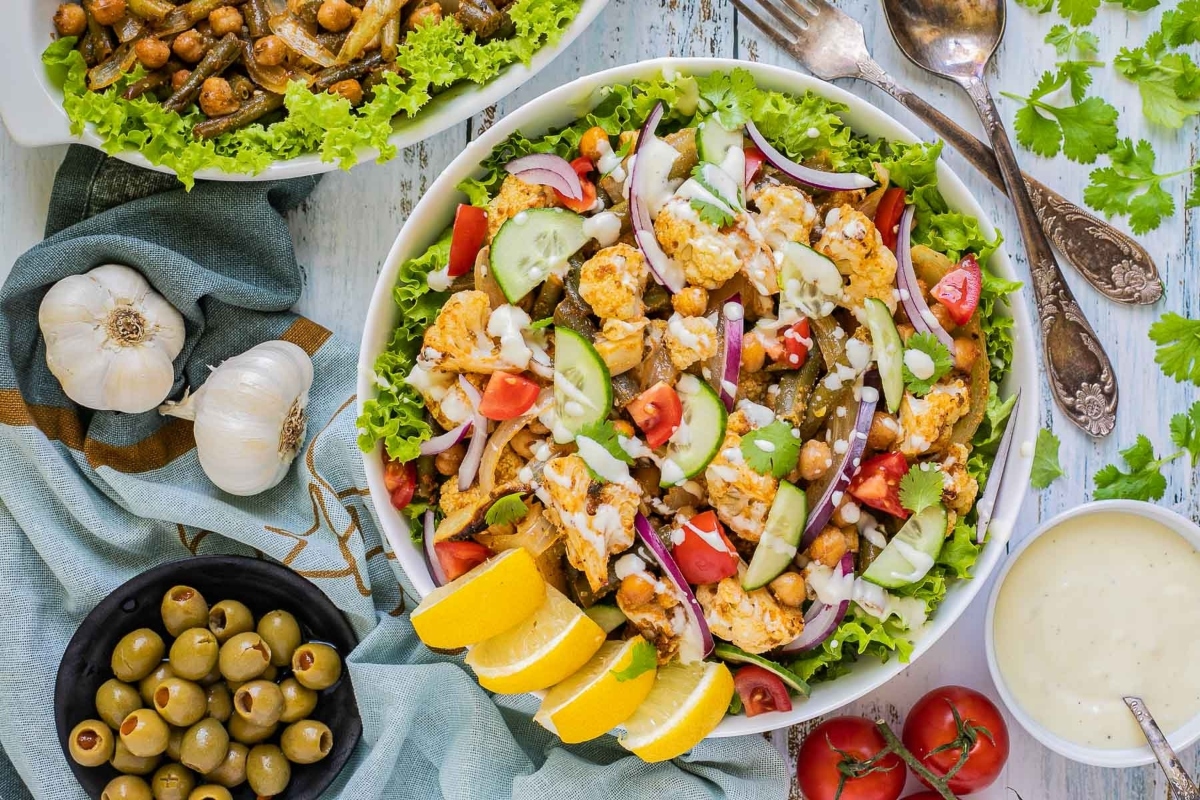 A salad with chickpeas, olives and tomatoes on a wooden table.
