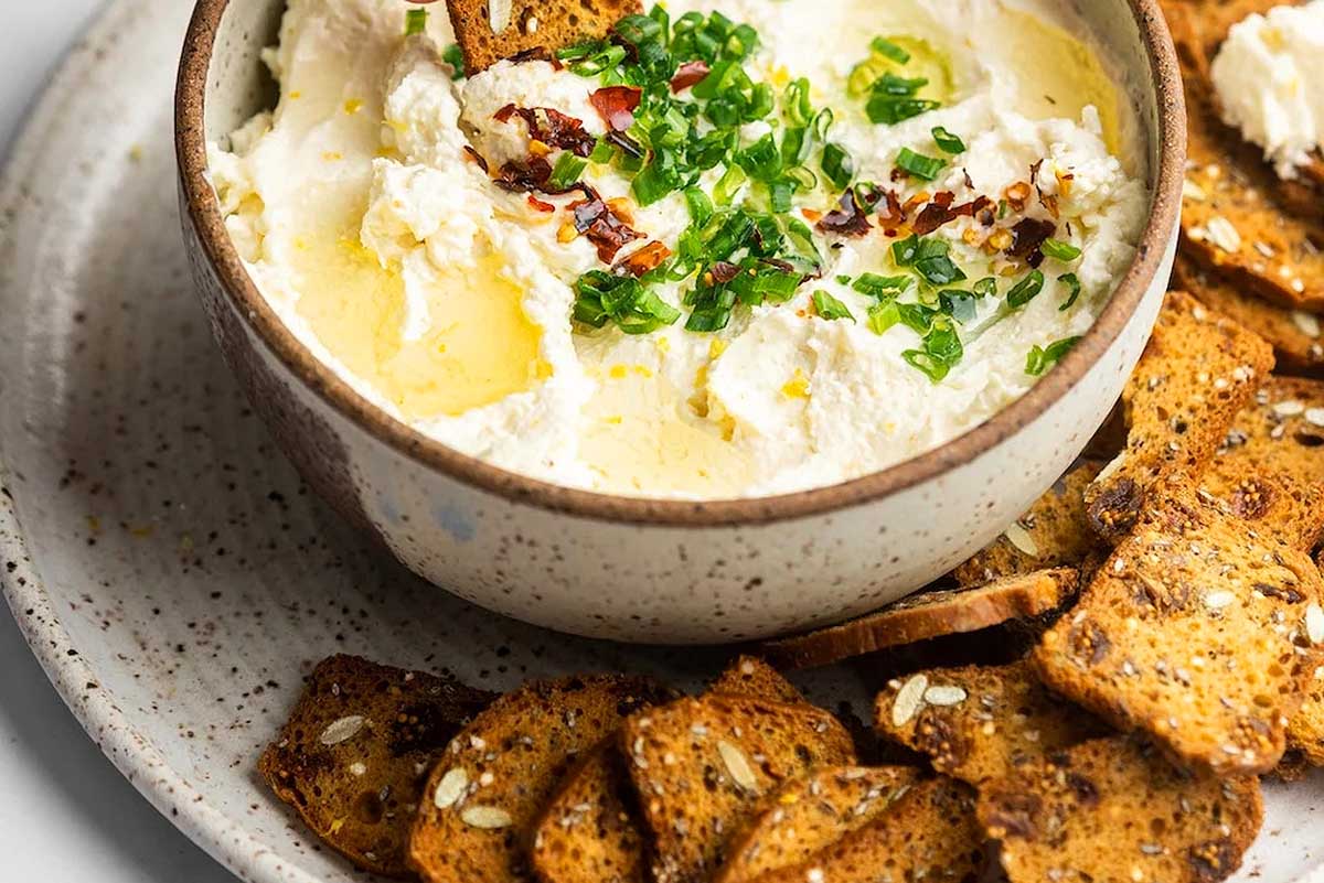A bowl of hummus with crackers on a white plate, perfect for a friends giving gathering.