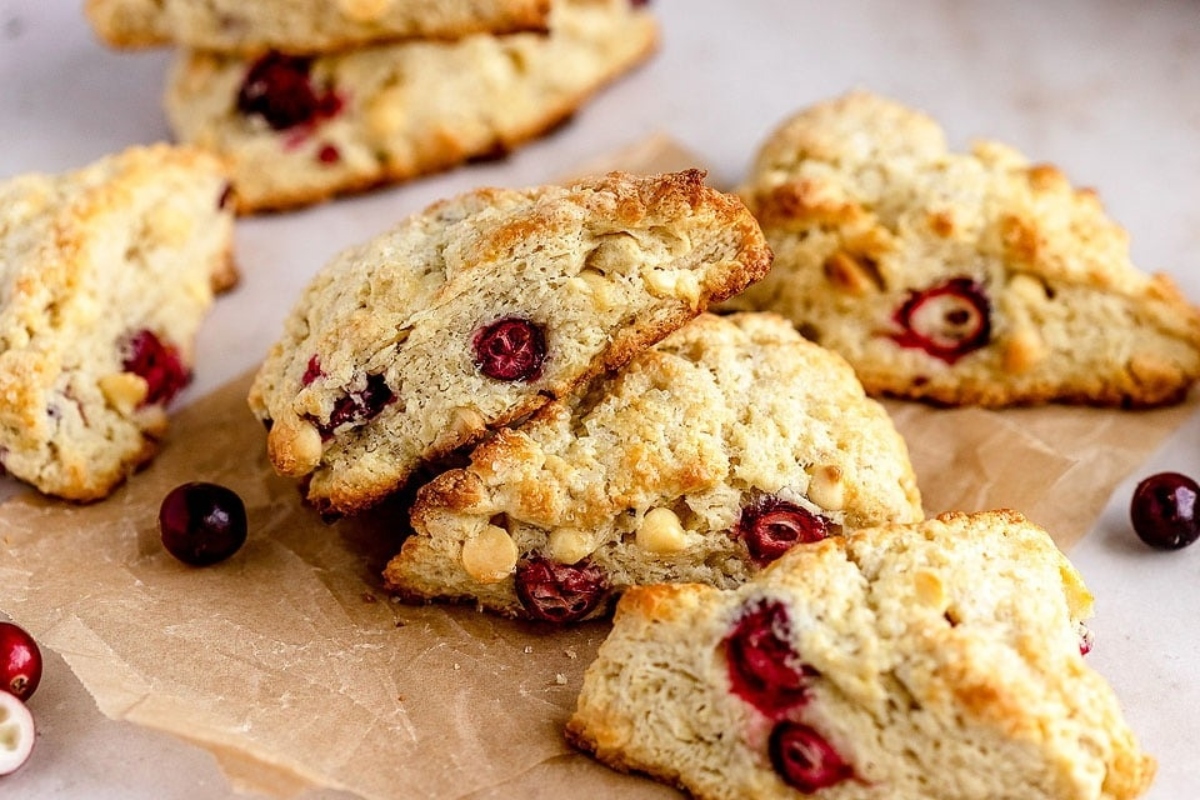A stack of cranberry scones on a piece of paper, topped with a drizzle of white chocolate.