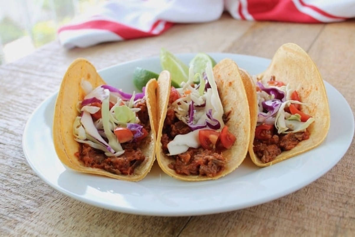 Three tacos, the easiest game day recipes, are sitting on a plate on a wooden table.