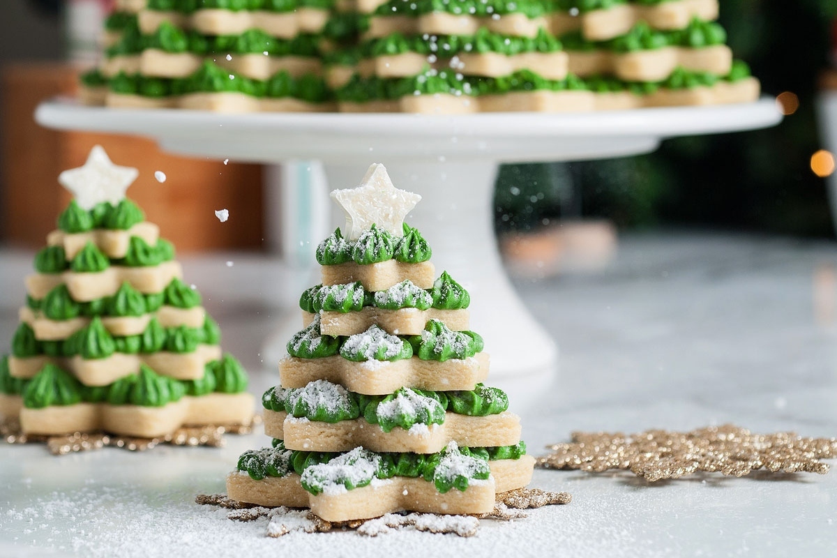 Sugar cookies cut out in the shape of Christmas trees arranged on a white plate.