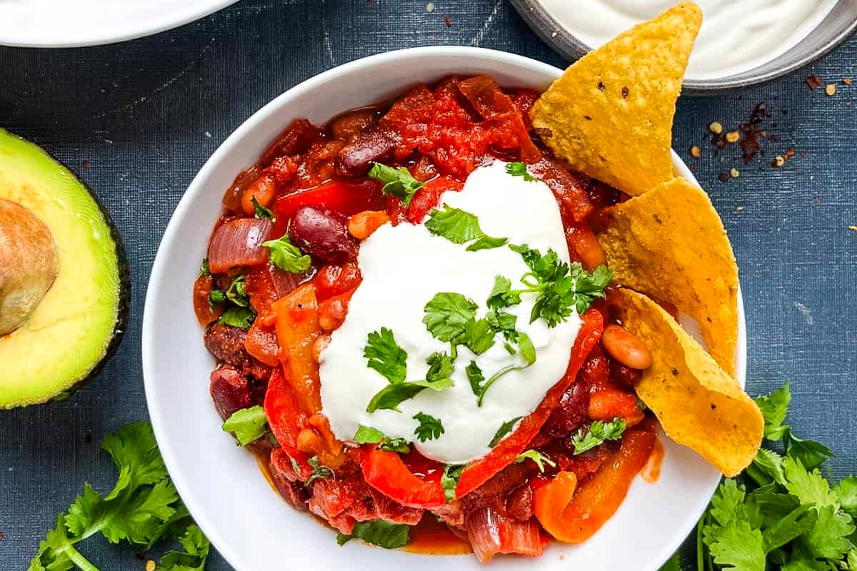 A delectable chili recipe featuring sour cream and accompanied by crispy tortilla chips.