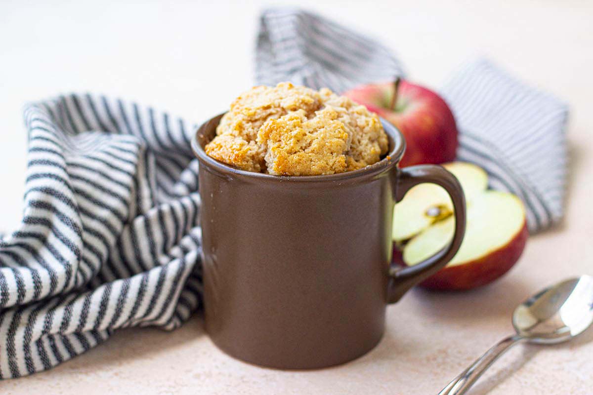 A mug with apples and a spoon, perfect for mug cake recipes.