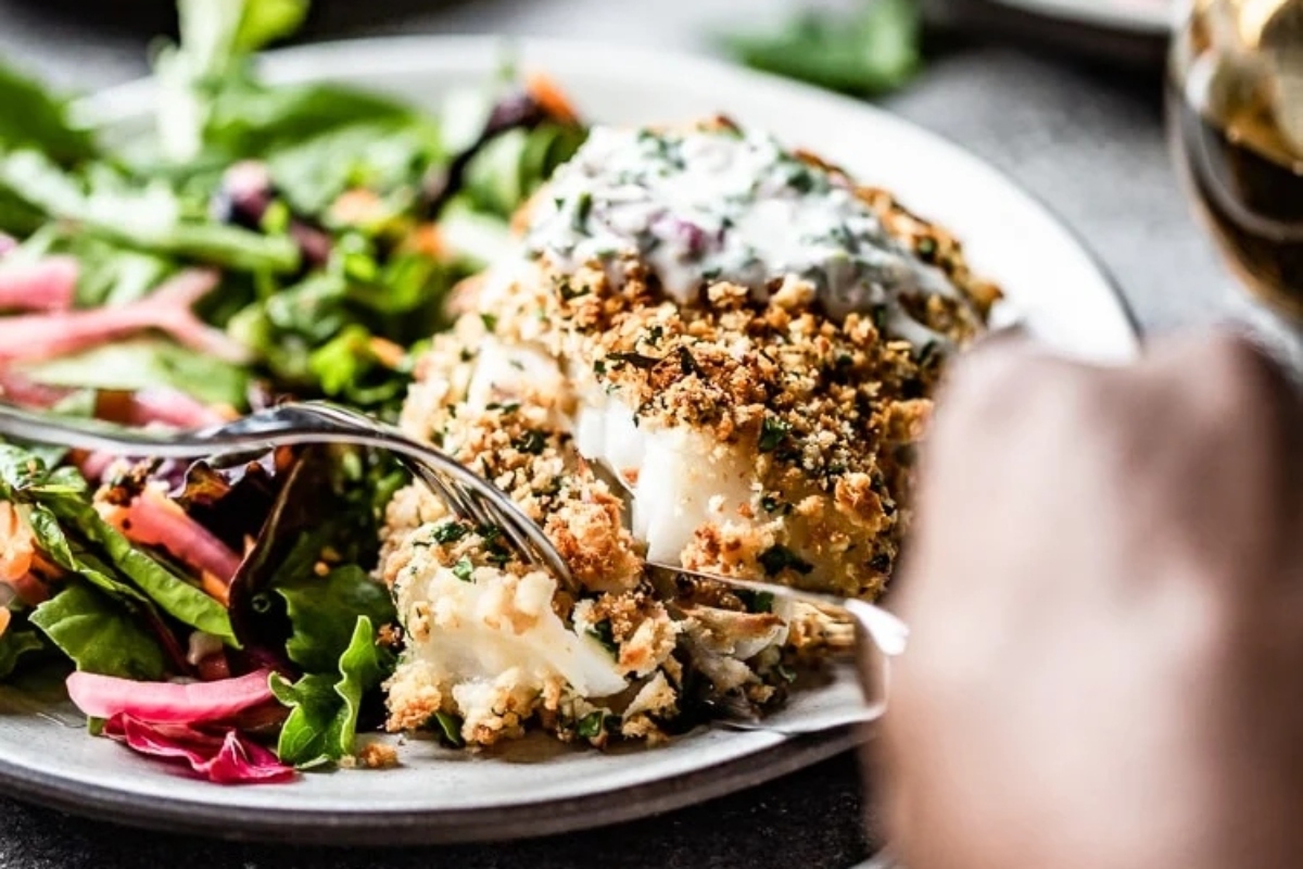 A person is preparing a delicious fish recipe, carefully balancing a plate of mouthwatering fish and fresh salad.