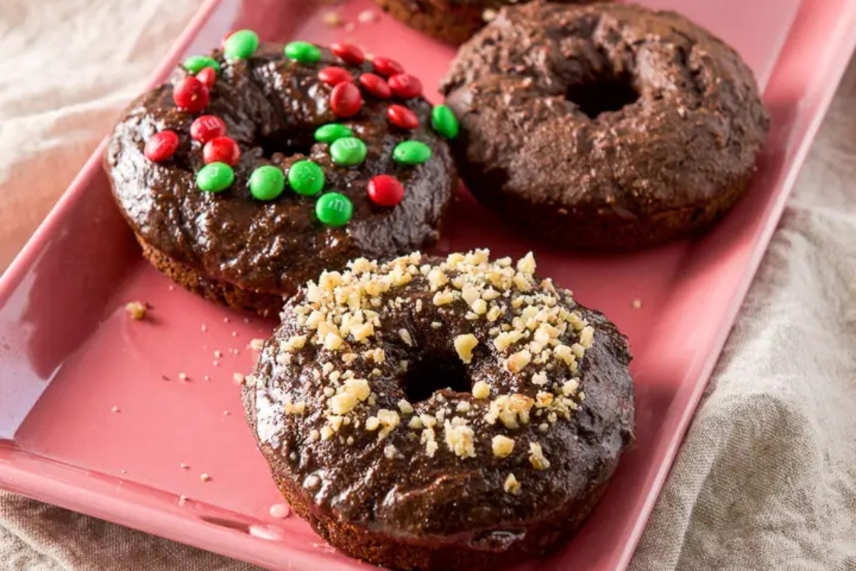 Three chocolate donuts on a pink plate, perfect for breakfast.