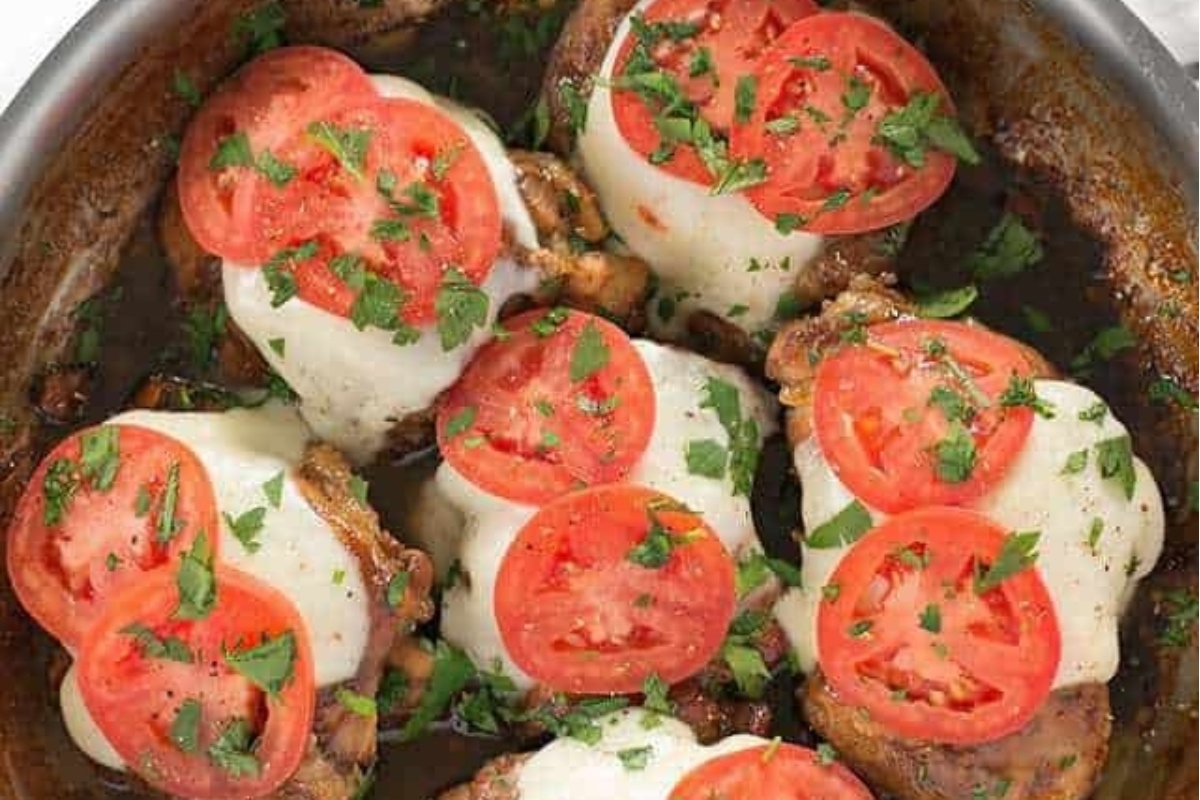 Chicken thighs cooked in a skillet with tomatoes and cheese.