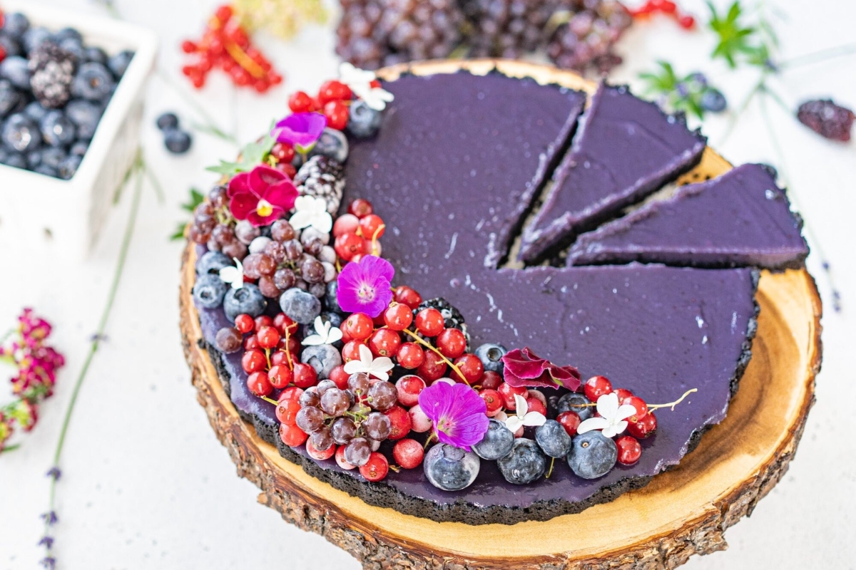 A mouthwatering purple tart with fresh berries and grapes beautifully arranged on a rustic wooden board. Indulge in this delectable treat, perfect for any occasion.