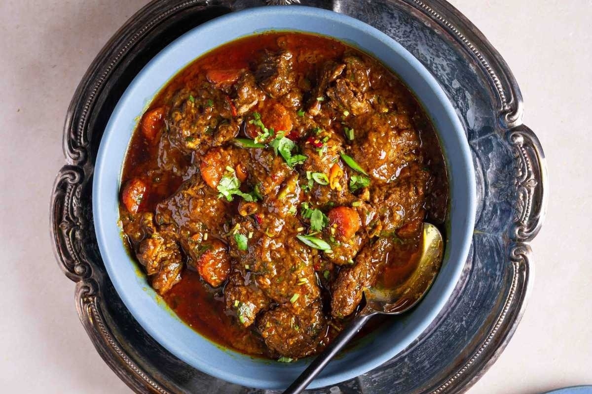 A flavorful bowl of stew on a table next to a spoon, perfect for cozy at-home recipes.