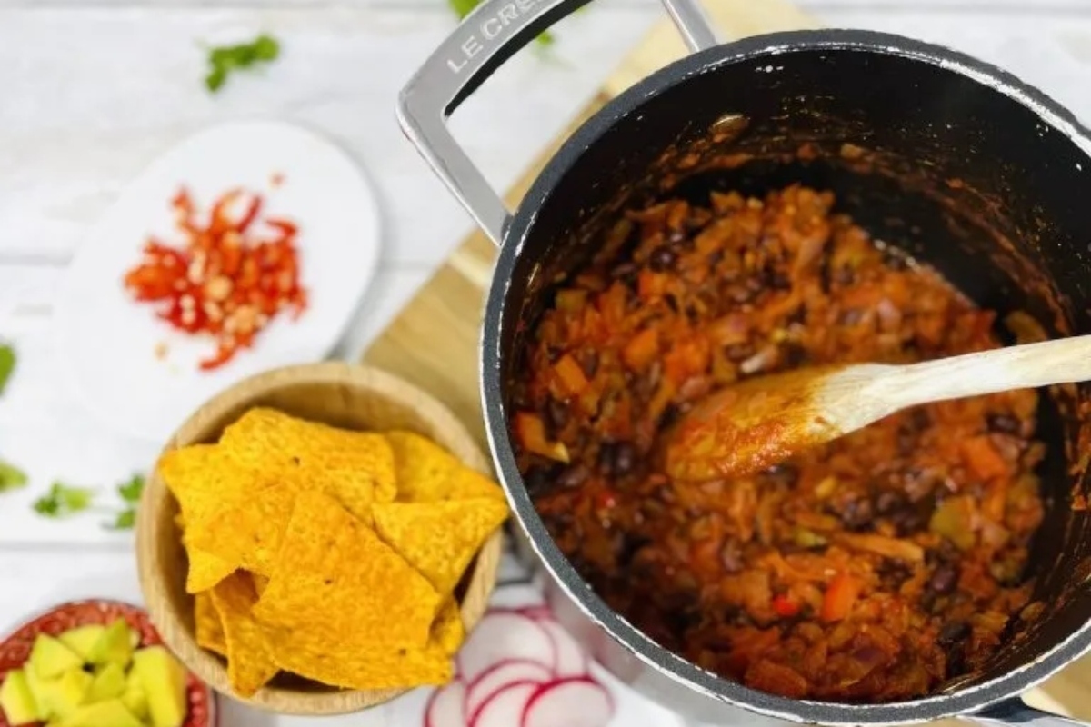 A loaded pot of vegetable chili with tortilla chips next to it.