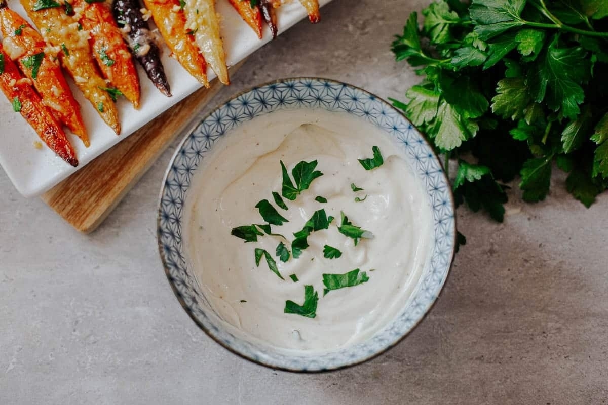 A bowl of dip with carrots, parsley, and truffle oil.