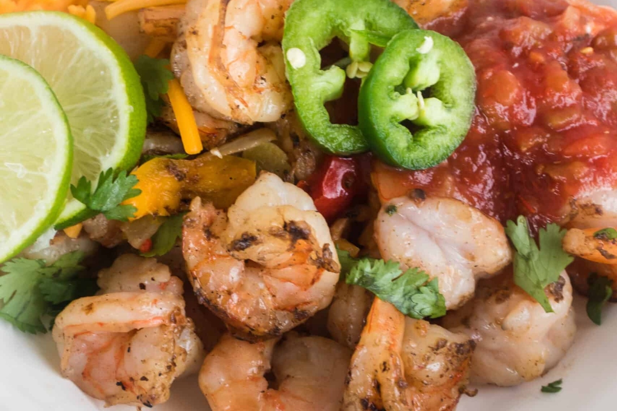A delicious shrimp dinner with salsa and lime wedges served on a plate.