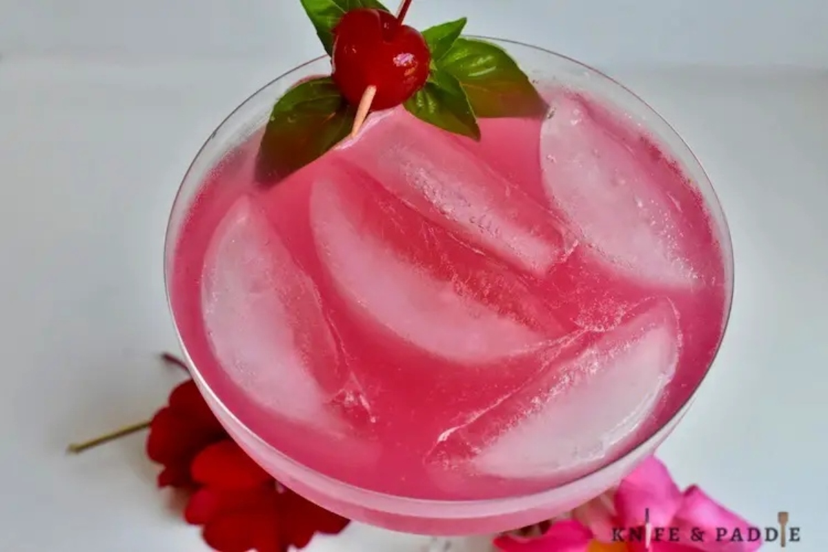 A pink Valentine's Day cocktail with ice and a cherry on top.