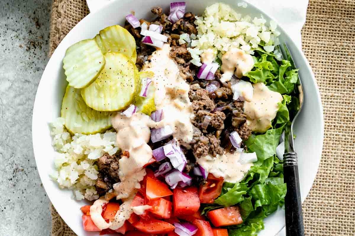A white bowl with lettuce, tomatoes, and pickles served as a refreshing grain bowl recipe.