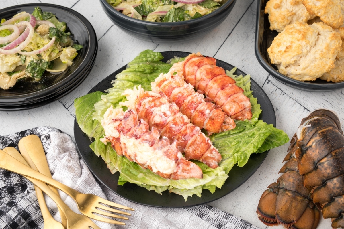 A simple, elegant plate of lobster, salad, and biscuits on a wooden table.