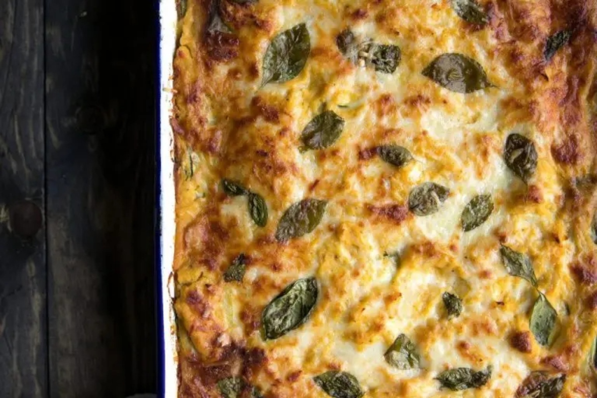 An inviting dish of lasagna with basil leaves on a wooden table, perfect for a make-ahead Thanksgiving recipe.