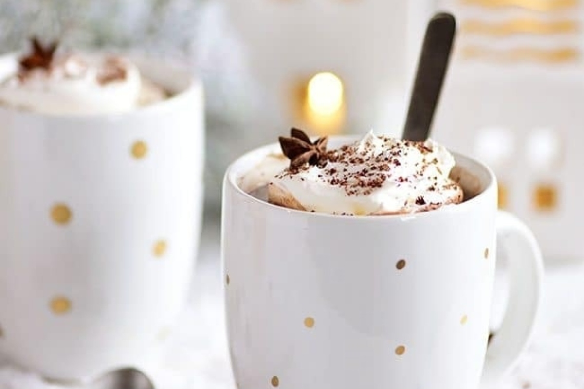 Two mugs of cocoa with whipped cream and a spoon.