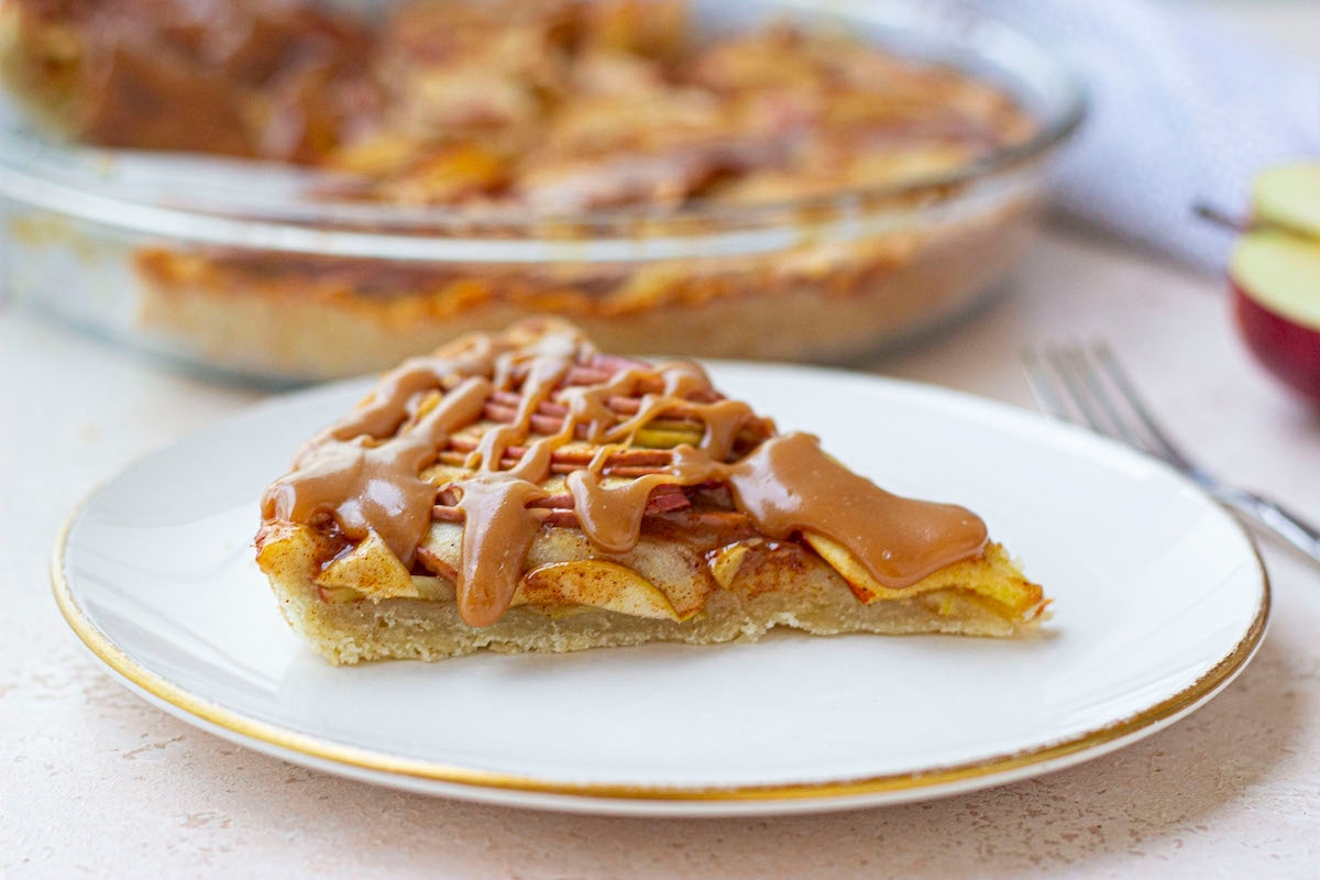 A slice of apple pie with caramel sauce on a tart.