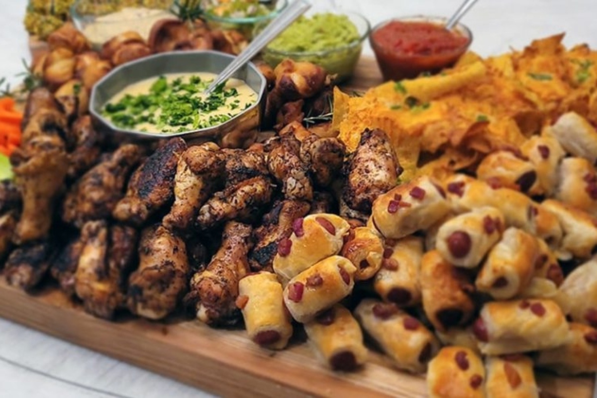 A tray of bite-sized appetizers and dips on a wooden board, perfect for game day.